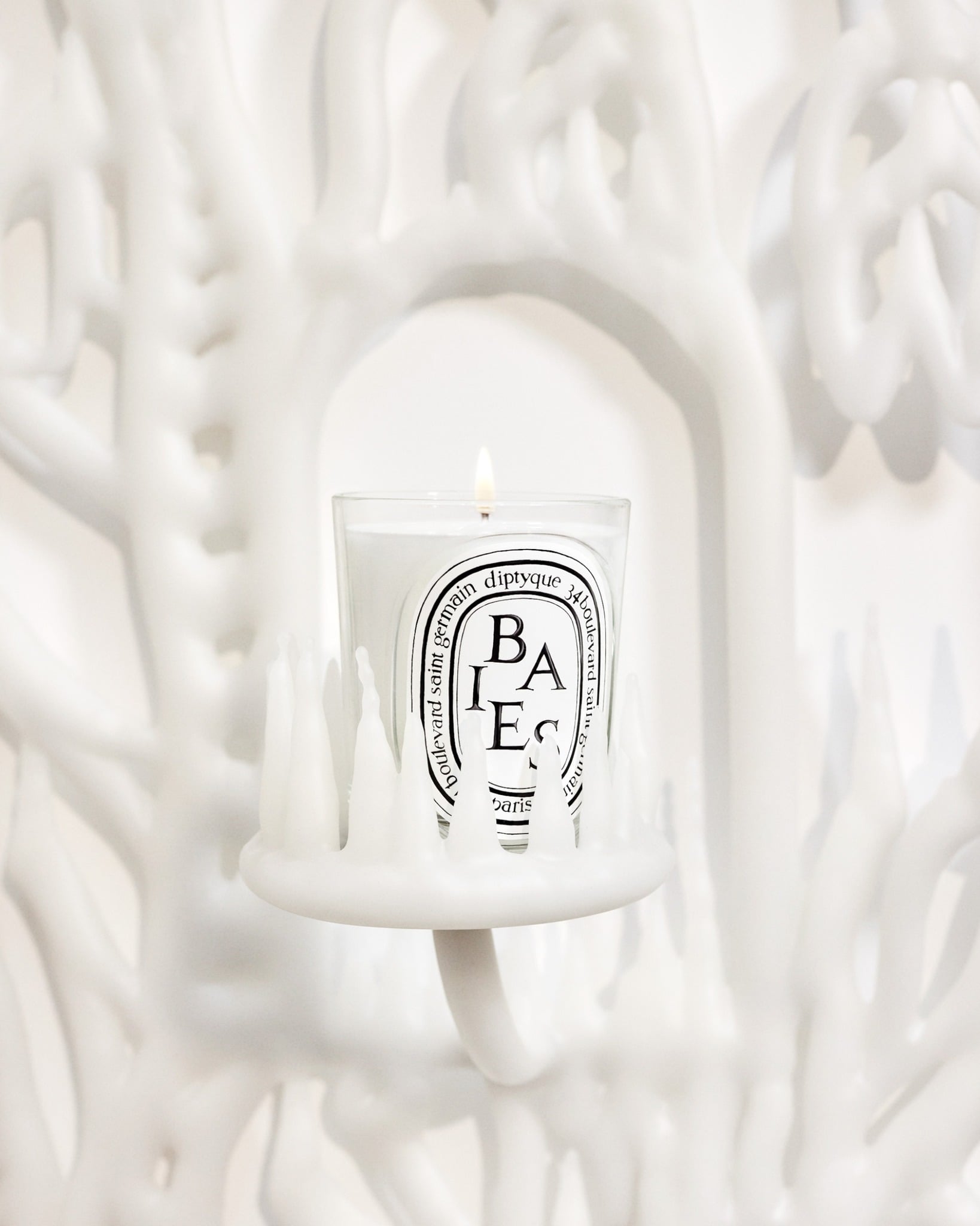 Lit Diptyque Baies candle against a white sculptural backdrop