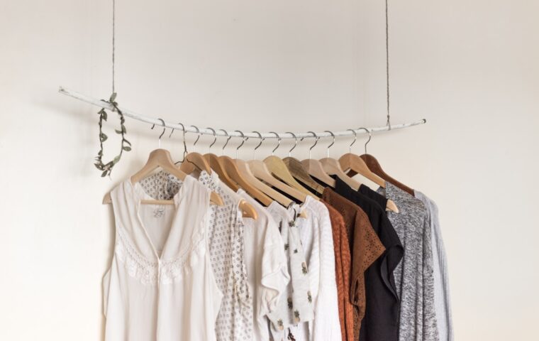 Neutral-toned clothing arranged on wooden hangers against a white wall