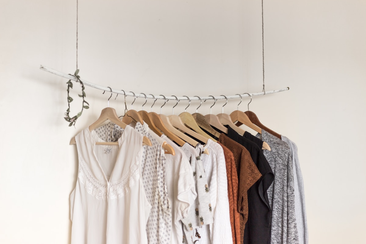 Neutral-toned clothing arranged on wooden hangers against a white wall
