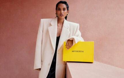 Model in a white suit holding a yellow Mytheresa shopping bag